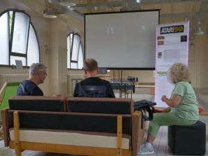 Drei Zuschauer vor Leinwand mit Spielstand 15:9 bei Atari-50-Event.