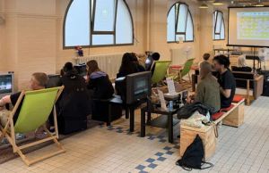 Menschen spielen Videospiele an alten Monitoren in einem Raum mit Liegestühlen und Projektionsfläche.