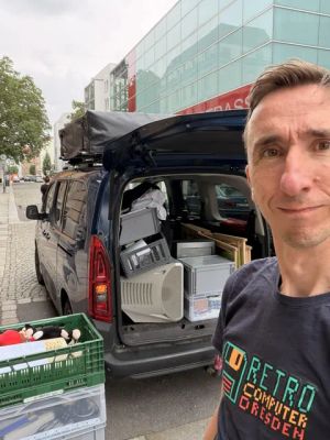 Mann im Retro-Computer-Dresden-Shirt vor einem mit alten Monitoren und Kisten gefüllten Van.
