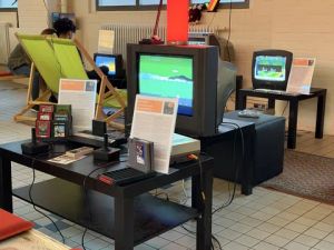 Retro-Gaming-Ausstellung mit Röhrenfernsehern, Nintendo-Konsolen, Controllern und Spielkassetten auf Tischen.